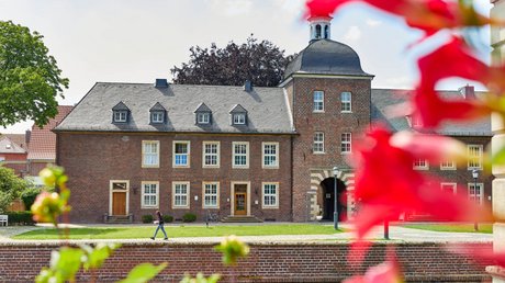 Appartementhotel Seeblick: Bildergalerie Rotes Backsteingebäude mit gewölbtem Turm vor blauem Himmel und Blumen im Vordergrund