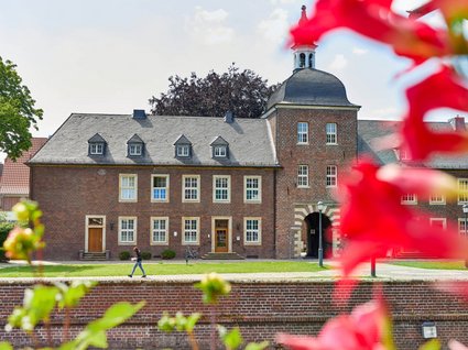 Seeblick: holidays by the lake in North Rhine-Westphalia Red brick building with arched tower and red flowers in foreground on a sunny day