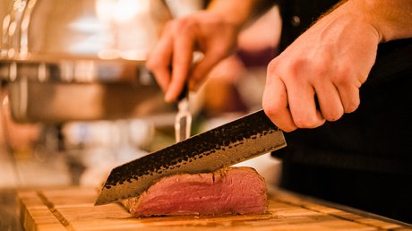 Appartementhotel Seeblick: Bildergalerie Persoon snijdt medium-rare gebakken vlees met een mes op een houten plank