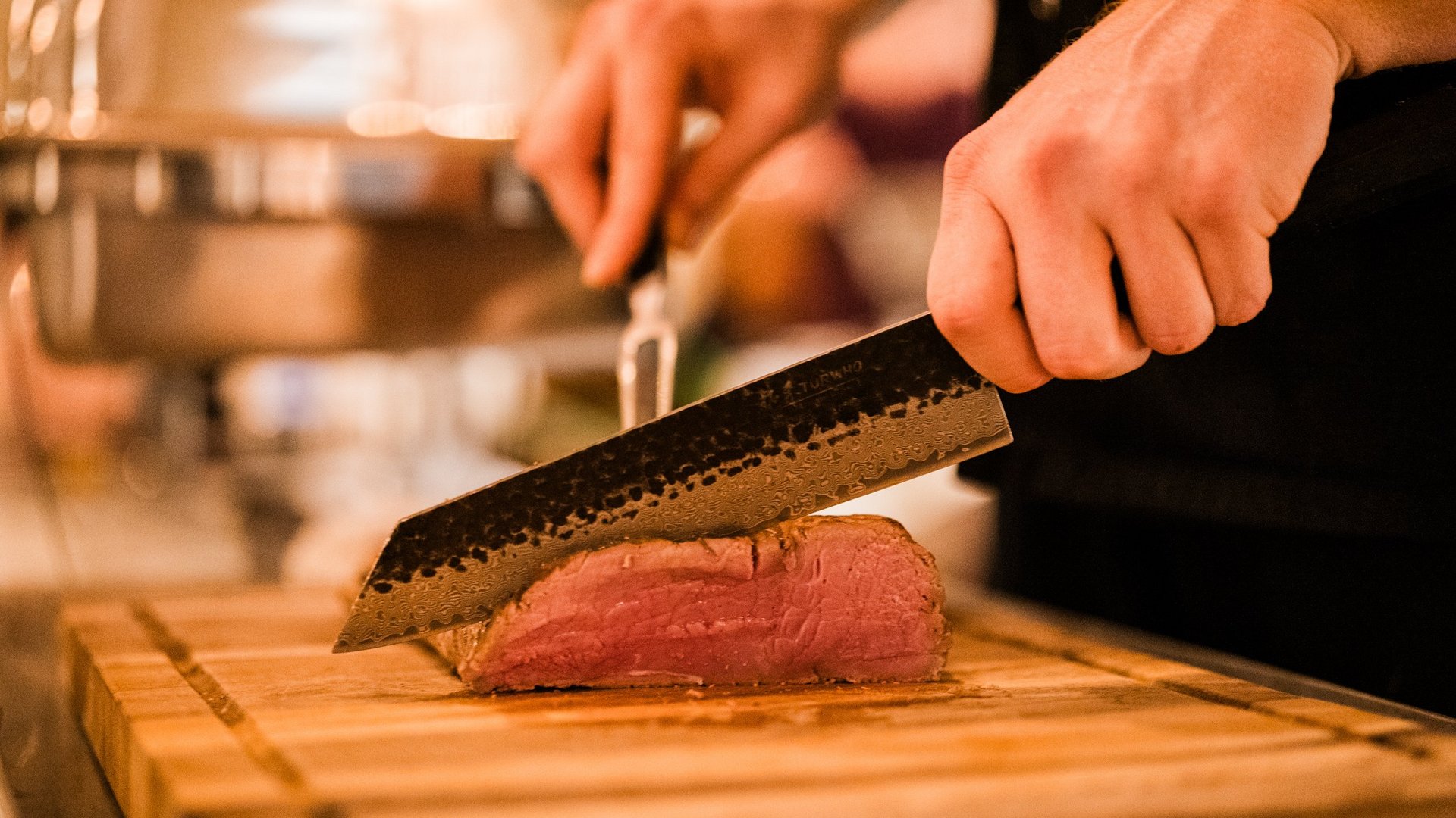Restaurant Seeblick: Speisekarte Person schneidet medium-rare gebratenes Fleisch mit Messer auf Holzbrett