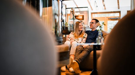 Appartementhotel Seeblick: Bildergalerie Paar sitzt entspannt und lächelnd auf Sofa in gemütlichem Raum