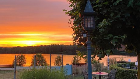 Appartementhotel Seeblick: Bildergalerie Sonnenuntergang über See mit Gartenmöbeln und Laterne im Vordergrund