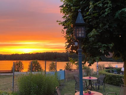 Hotel Seeblick in Gronau Sonnenuntergang über See mit Gartenmöbeln und Laterne im Vordergrund