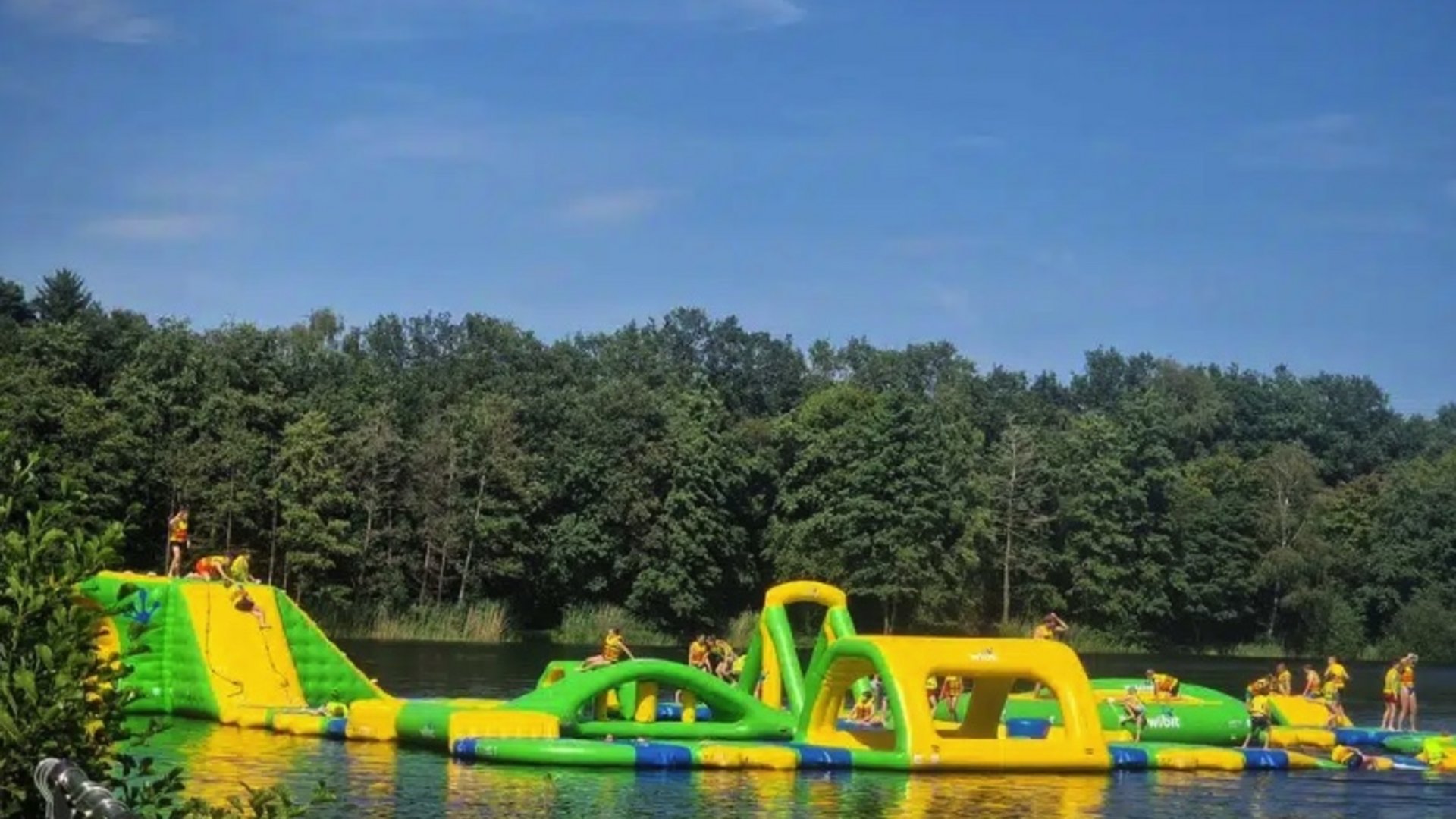 Erholung, Abenteuer und Badespaß für die ganze Familie – direkt am Dreiländersee Aufblasbarer Wasserpark mit Kletterelementen auf einem See vor Waldkulisse