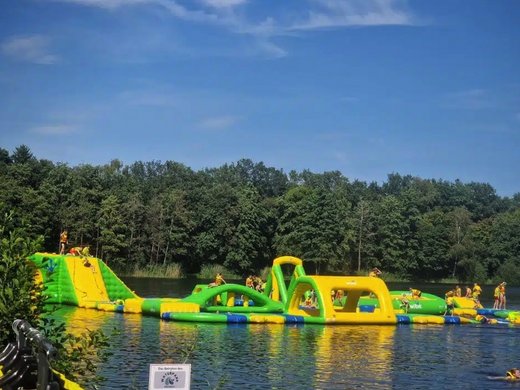 Erholung, Abenteuer und Badespaß für die ganze Familie – direkt am Dreiländersee Aufblasbarer Wasserpark mit Kletterelementen auf einem See vor Waldkulisse