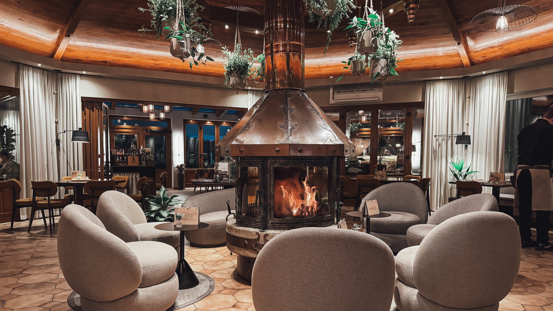 Restaurant Gronau: Seeblick Cozy seating area with round fireplace and hanging plants in a restaurant
