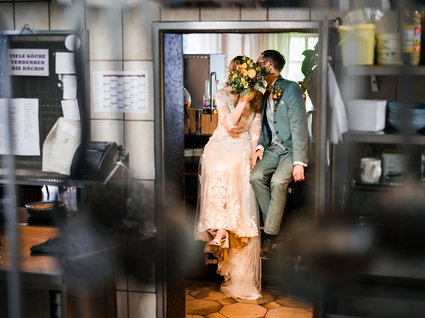News vom Hotel direkt am See in NRW Braut und Bräutigam verstecken ihr Gesicht hinter einem Blumenstrauß in einer Küche