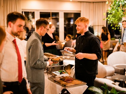 News vom Hotel direkt am See in NRW Mann in schwarzer Kochjacke serviert Fleisch bei Buffet im Restaurant